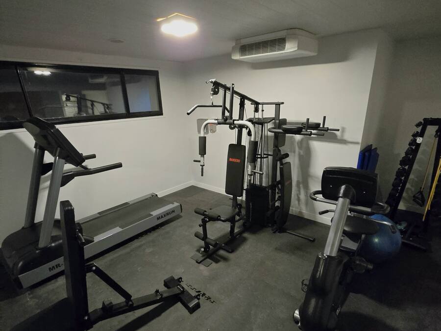 A home gym with a treadmill, weight bench, and various exercise equipment.