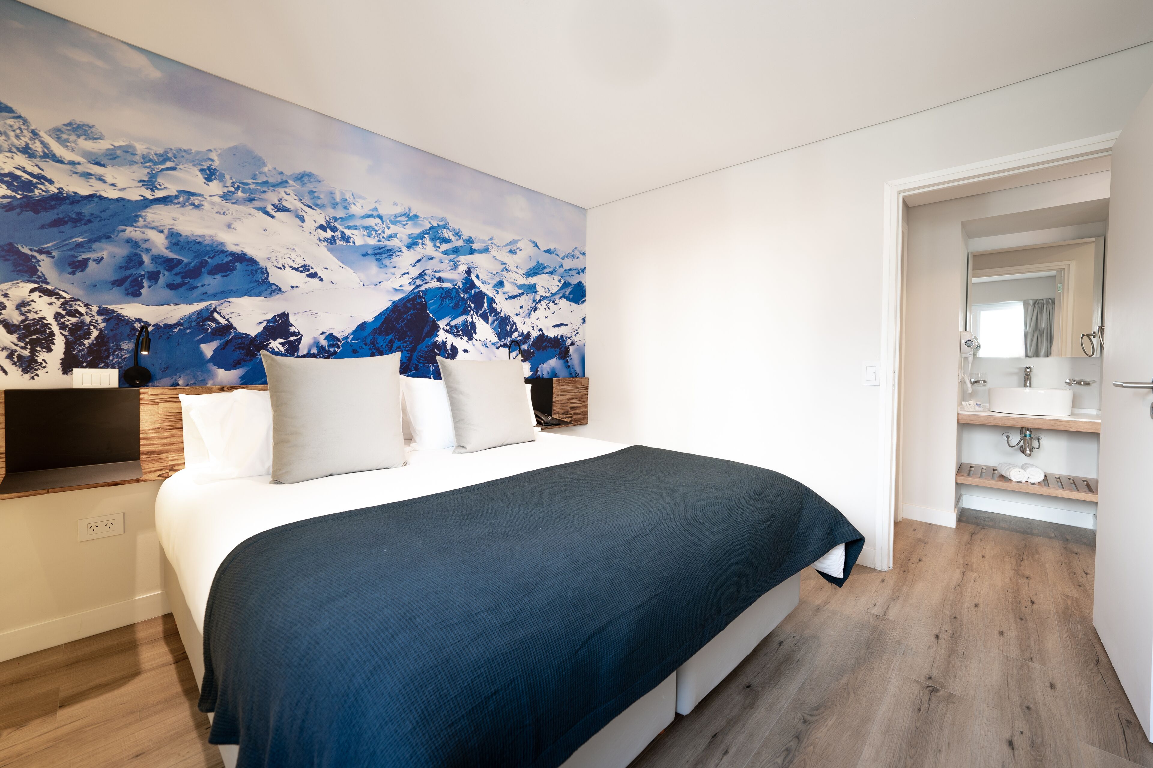 Un dormitorio con una cama grande, un televisor montado y un mural con un paisaje de montaña en la pared.