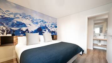 Un dormitorio con una cama grande, un televisor montado y un mural con un paisaje de montaña en la pared.