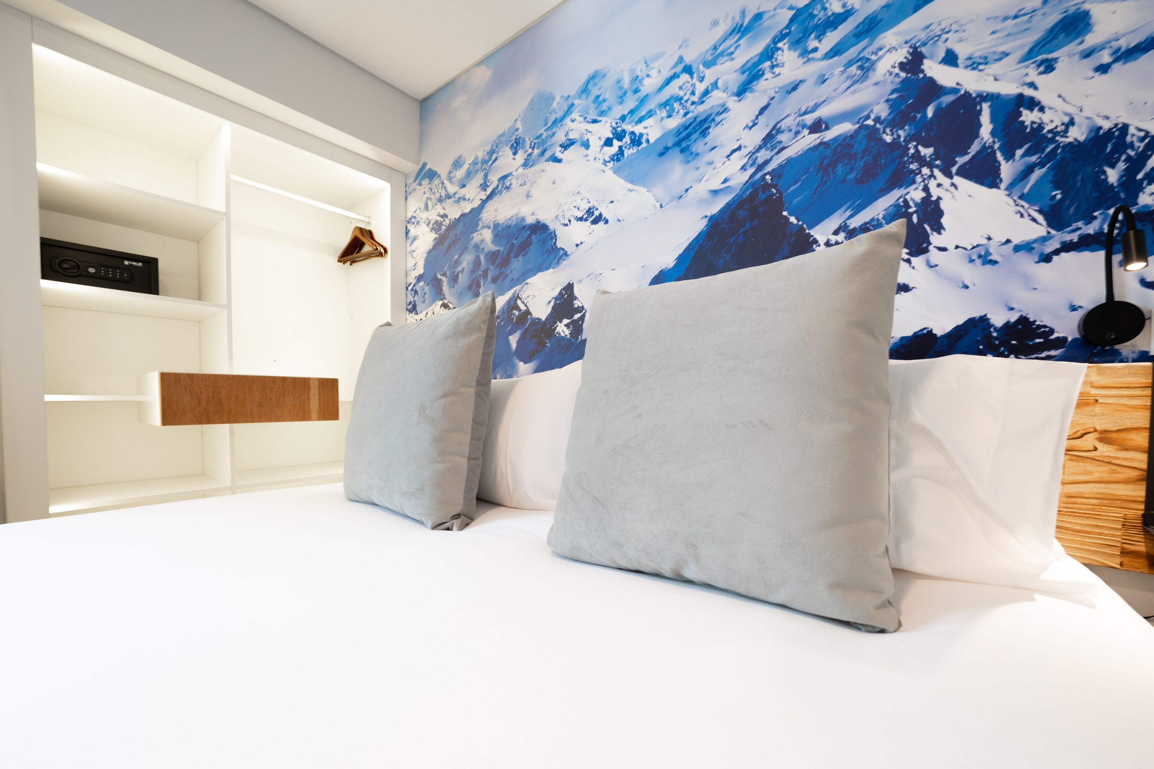 A bedroom with a mountain-themed wall mural, a bed with white bedding, and a wooden nightstand.