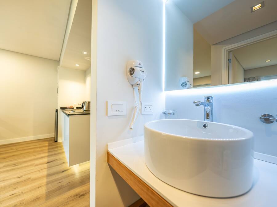 A modern bathroom with a large white sink, a hairdryer mounted on the wall, and a mirror above the sink.