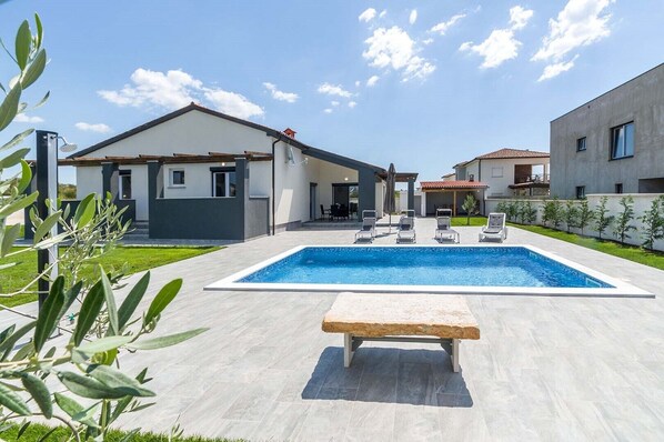 A modern house with a swimming pool, a covered patio, and a garden.