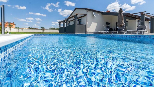 A swimming pool with clear blue water, a covered patio area with lounge chairs, and a building with a white facade in the background. - Villa Marino with private pool (Vodnjan)