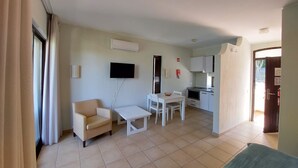 A living room with a sofa, a TV, a dining table, and a kitchen area with cabinets and a stove. - CASA da PRAIA ALBUFEIRA PORTUGAL (Albufeira)