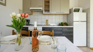 A modern kitchen with white cabinets, a microwave, and a refrigerator. There is a dining table with plates, a vase with flowers, and a wine bottle. - Apartment Matej (Rabac)