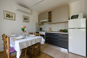 A compact kitchen with a dining area, featuring a white refrigerator, a microwave, a stove, and a sink. There are framed pictures on the wall and a table set for dining.