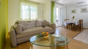 A living room with a sofa, a glass coffee table with fruit, a dining table with chairs, and a view of the outdoors. - Apartment Matej (Rabac)