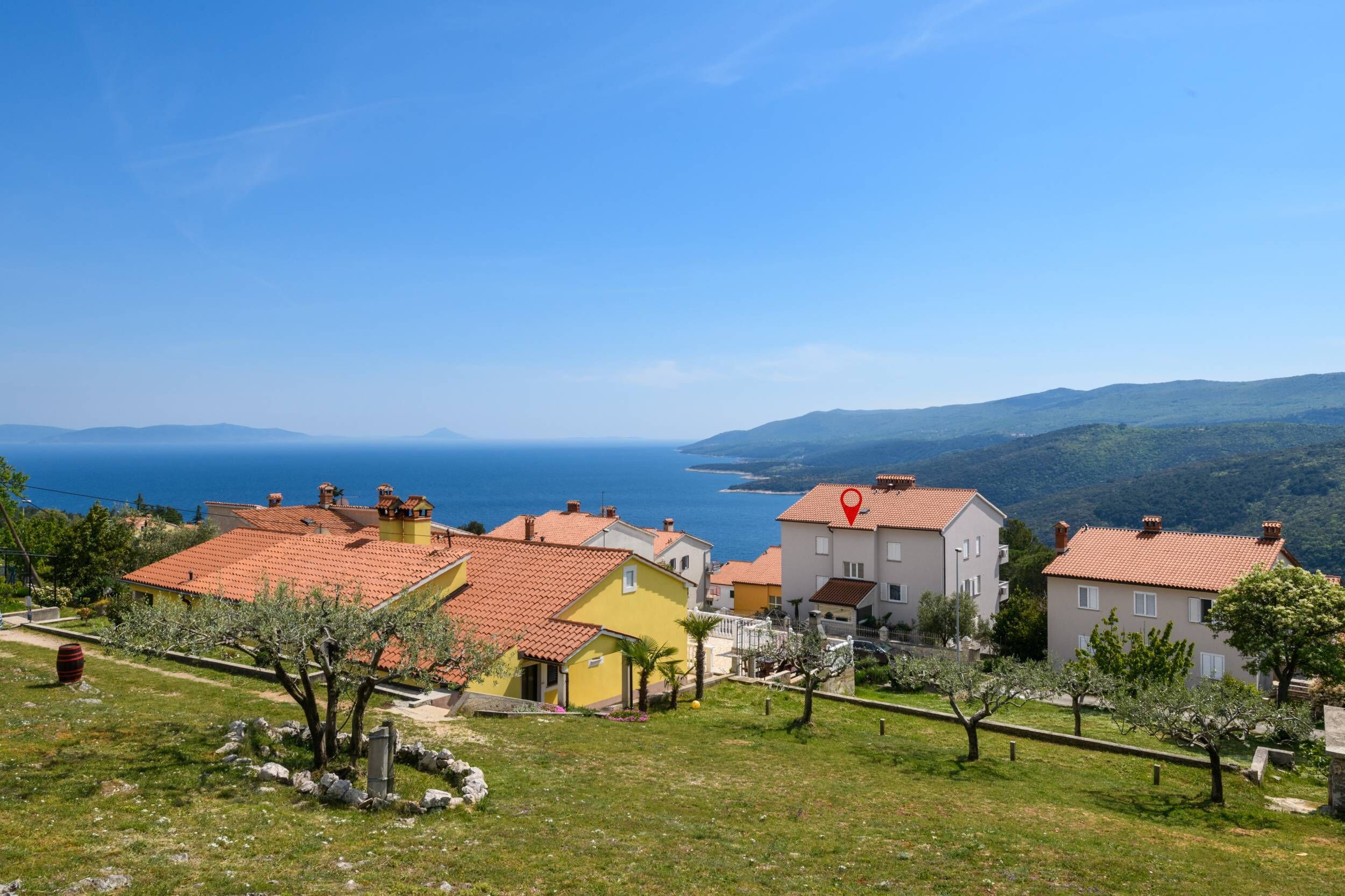 A coastal village with terracotta-roofed houses, a clear blue sky, and a view of the sea.