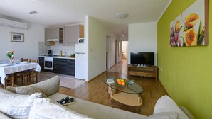 A living room with a glass coffee table, a sofa, a TV, and a kitchen in the background. - Apartment Matej (Rabac)