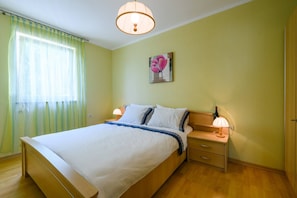 A bedroom with a bed, bedside tables, a lamp, a painting, and a window with curtains.