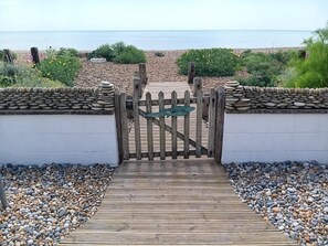Une porte en bois mène à une plage de galets d’où l’on a une vue sur la mer.