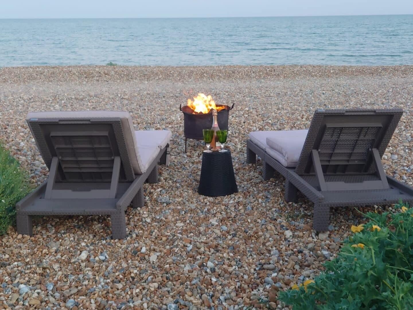 Una playa de guijarros con dos sillas de descanso y una chimenea central.