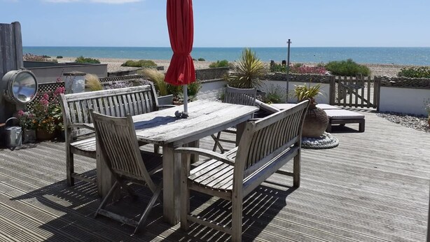 Een houten terras met een tafel, stoelen en een rode parasol, met uitzicht op de zee.
