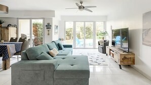 Una sala de estar moderna con un sofá modular gris, un televisor de pantalla plana y un ventilador de techo.