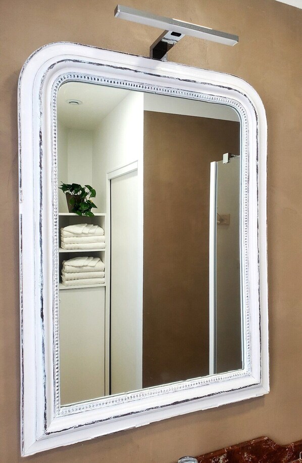 A bathroom with a white-framed mirror, a towel rack with folded towels, and a plant.