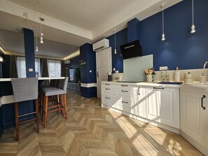 A modern kitchen with white cabinets, a herringbone floor, and pendant lighting.