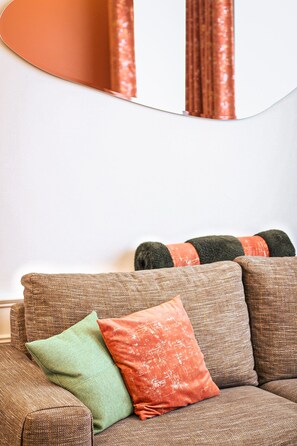 Ein Wohnzimmer mit einem braunen Sofa und drei Kissen in Grün, Orange und Schwarz.