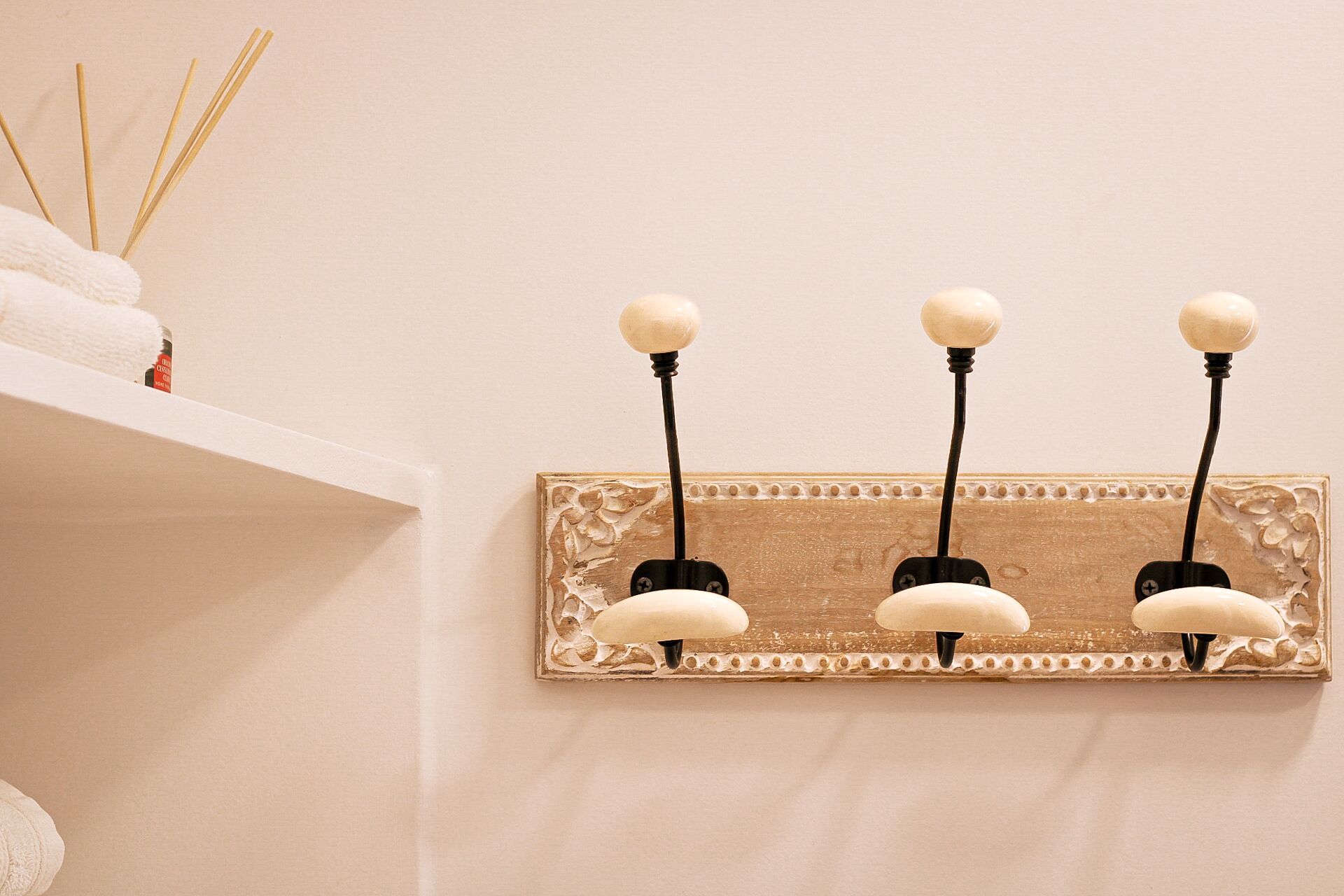Wandlamp met drie bolvormige lampen, een gestructureerd paneel en een wit plankje met een handdoek en een rietverfrisser.