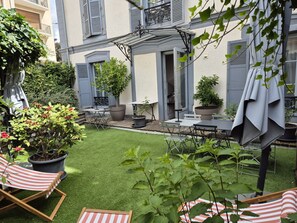 Un patio con un pequeño césped, mobiliario exterior y plantas en macetas.