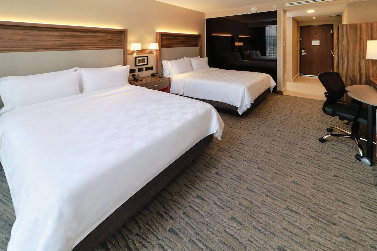 Une chambre d’hôtel avec deux lits, un bureau, une chaise et une porte donnant sur une pièce sombre.