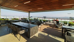 An outdoor patio with a wooden ceiling, seating arrangements, and a view of the airport in the background. - Holiday Inn Hotel and Suites Mexico Felipe Angeles Airport by IHG (Zumpango)