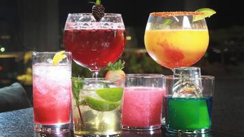 Variedad de cócteles coloridos en distintos vasos, algunos adornados, sobre una barra.