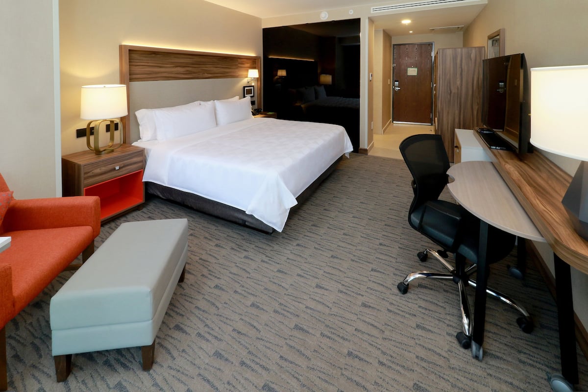 Une chambre d’hôtel avec un grand lit, un bureau avec une chaise, un petit fauteuil orange et une télévision.