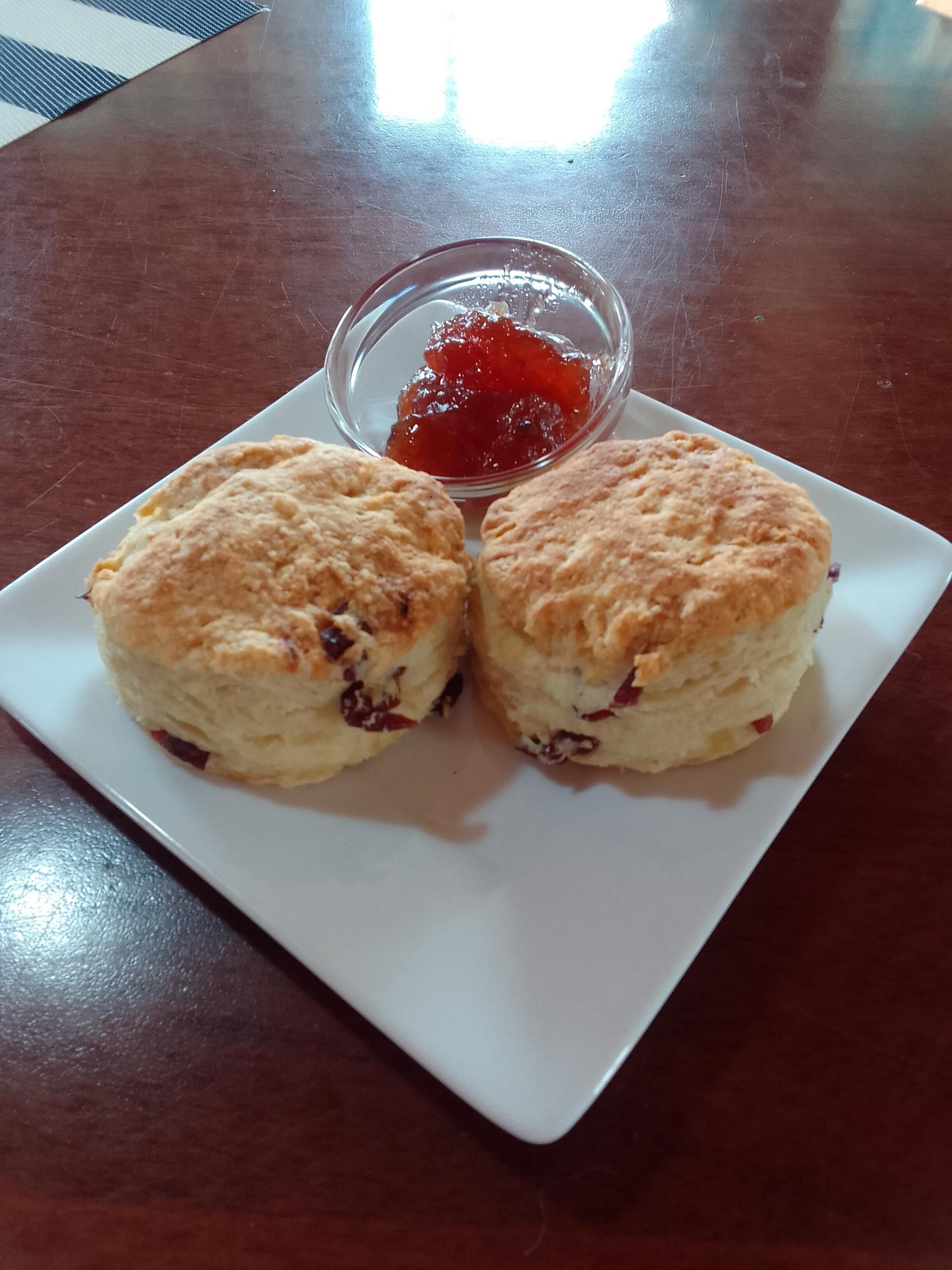 Dos scones sobre un plato blanco con un recipiente pequeño de mermelada.