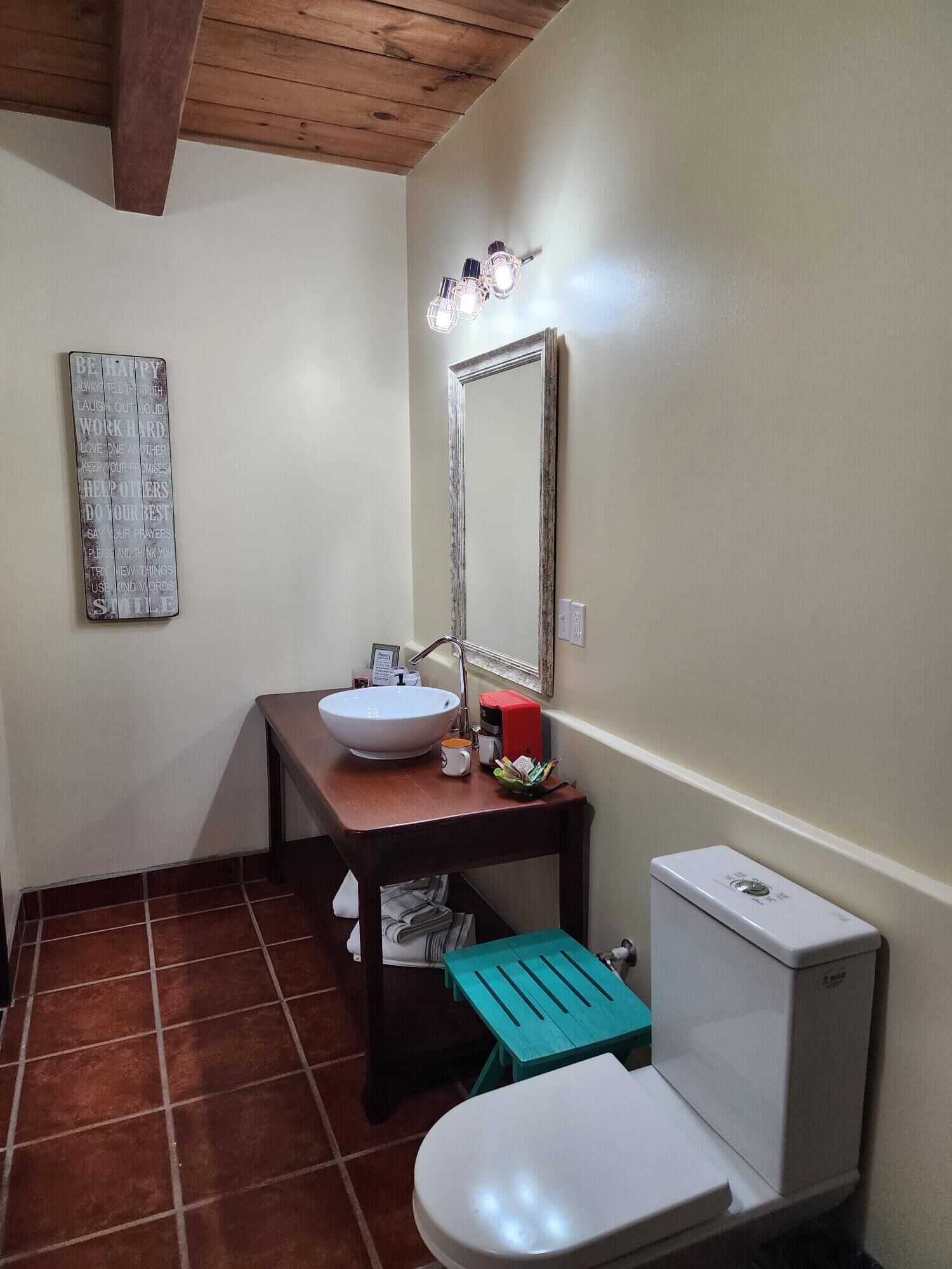 A bathroom with a white sink, a mirror, a toilet, and a small stool.