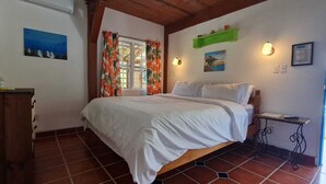 Un dormitorio con una cama, una mesita de noche, un aparador y una ventana con cortinas.