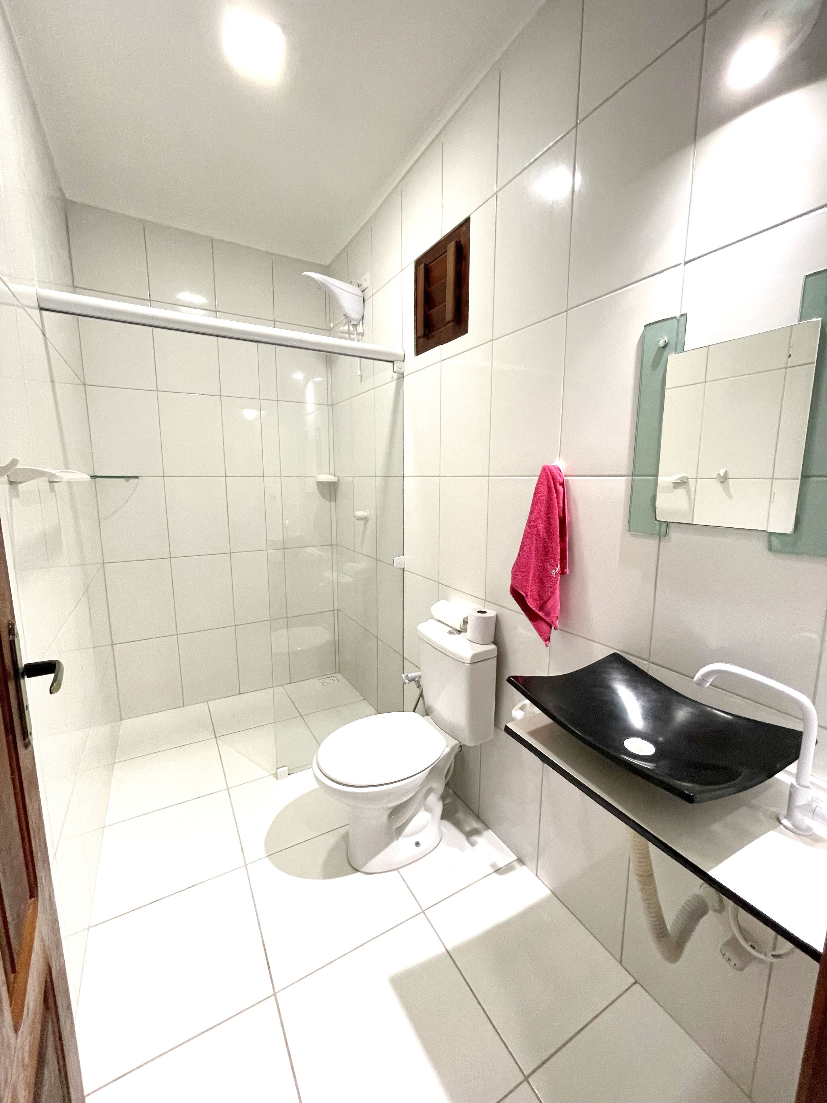 Une salle de bain moderne avec une douche à parois de verre, des toilettes blanches et un lavabo noir doté d’un plan de toilette en verre.