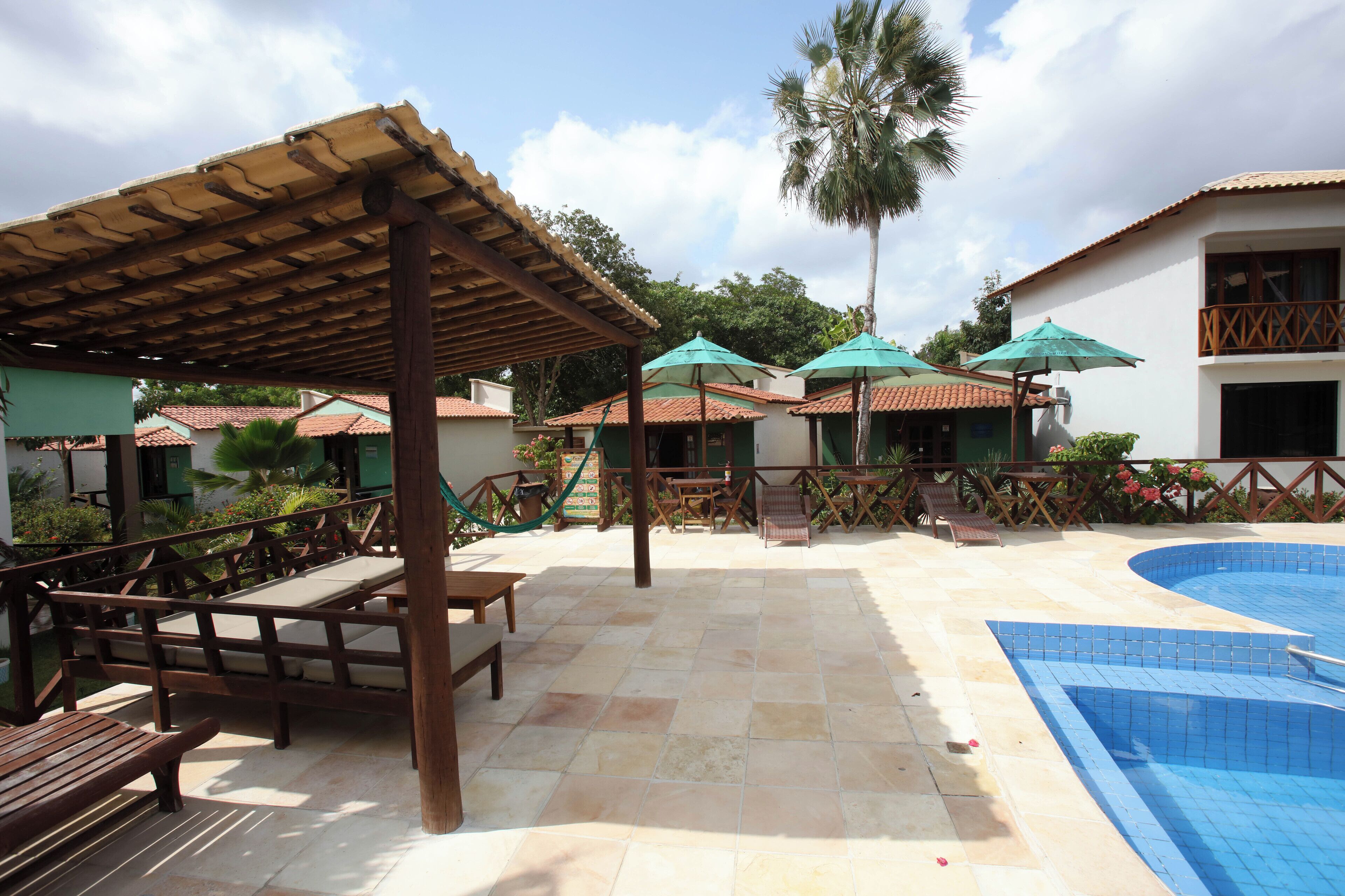 A pool area with a wooden pergola, lounge chairs, and umbrellas.