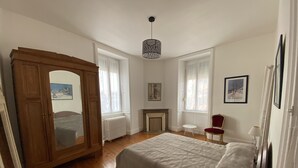 A bedroom with a large bed, a wooden wardrobe, a small table, a chair, and a fireplace. - SEASONAL HOUSE RENTAL (Les Sables-d'Olonne)