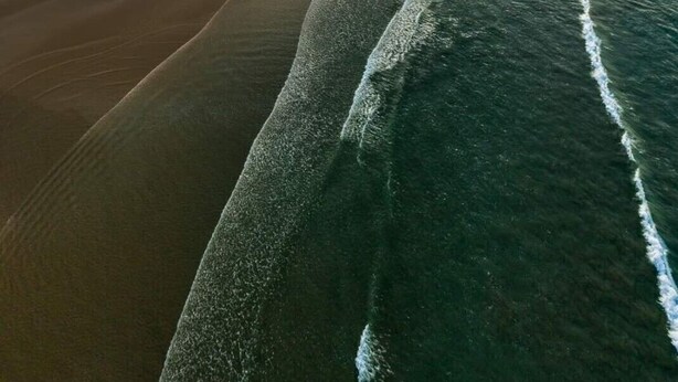 An aerial view of a beach with a wide expanse of sand and gentle waves. - SEASONAL HOUSE RENTAL (Les Sables-d'Olonne)