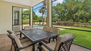 An outdoor patio with a table and chairs, a ceiling fan, and a view of a swimming pool and greenery. - Homestead Laurel: Private Pool, Water Park, Golf View, Near Disney (Kissimmee)