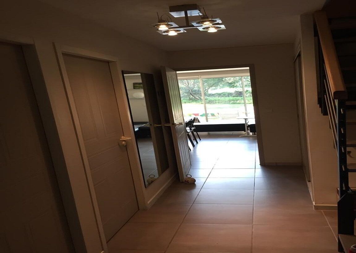 Un couloir avec une porte à gauche, une fenêtre à droite et un escalier sur le côté droit.