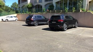 Ein Parkplatz mit zwei SUVs und einem weißen Auto vor einem Gebäude mit Balkon.