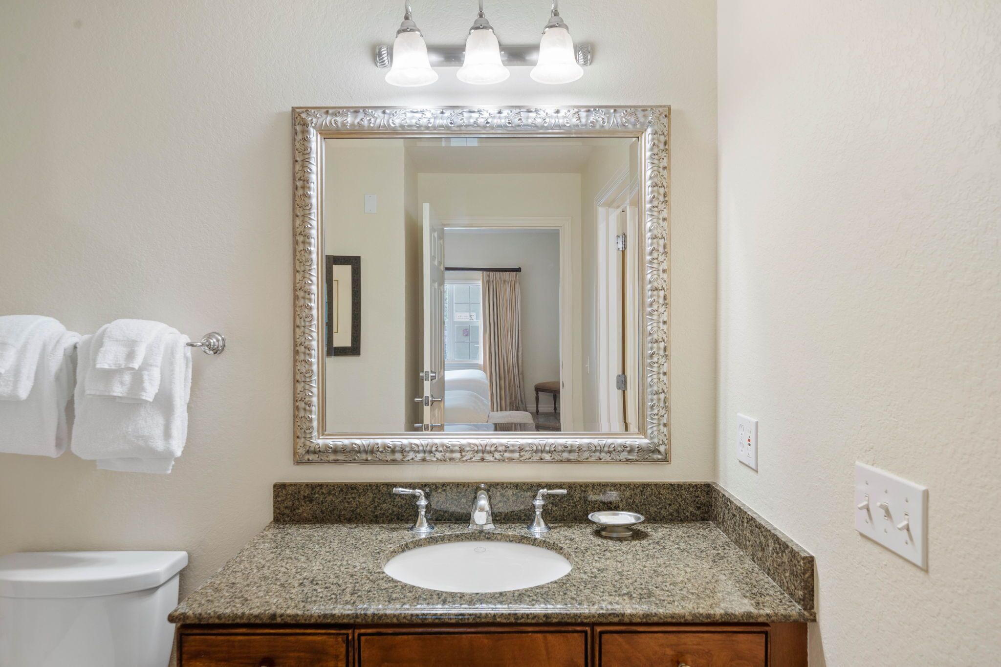 A bathroom with a granite countertop sink, a large mirror, and a toilet.