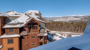 A large lodge with multiple wooden structures, a ski slope in the background, and a clear view of the surrounding mountains.
