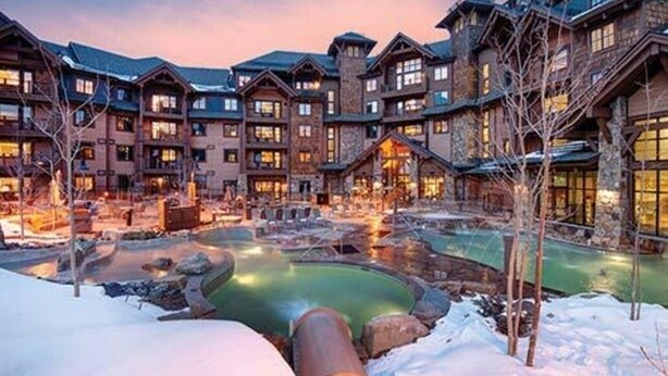 A lodge with multiple wooden buildings, a central heated pool, and a snowy ground.