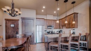 A kitchen with wooden cabinets, a stainless steel refrigerator, and a dining area with wooden chairs.