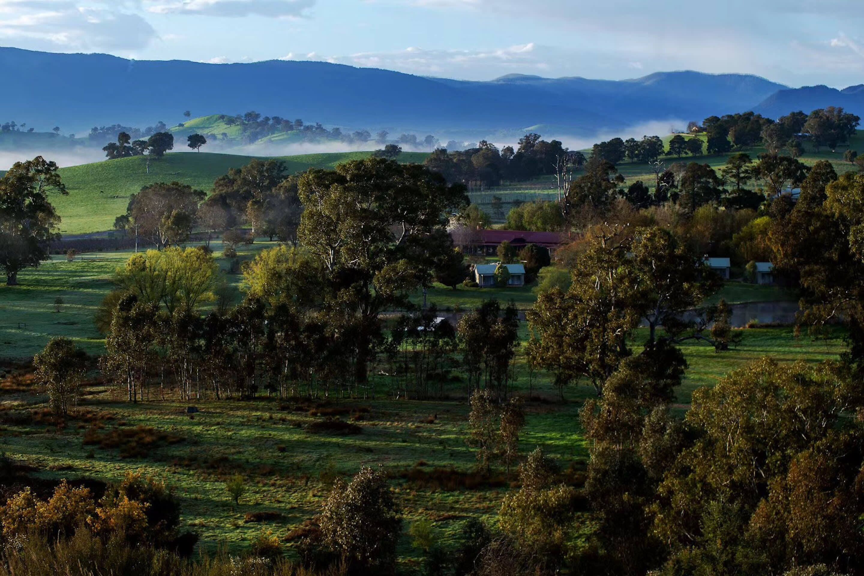 A rural landscape with rolling hills, scattered trees, and a few buildings.