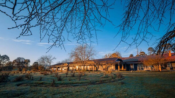 A large building with multiple sections, surrounded by a grassy area with sparse trees.