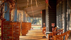 Un espace extérieur abrité, avec des piliers en briques, des tables et des chaises en bois.