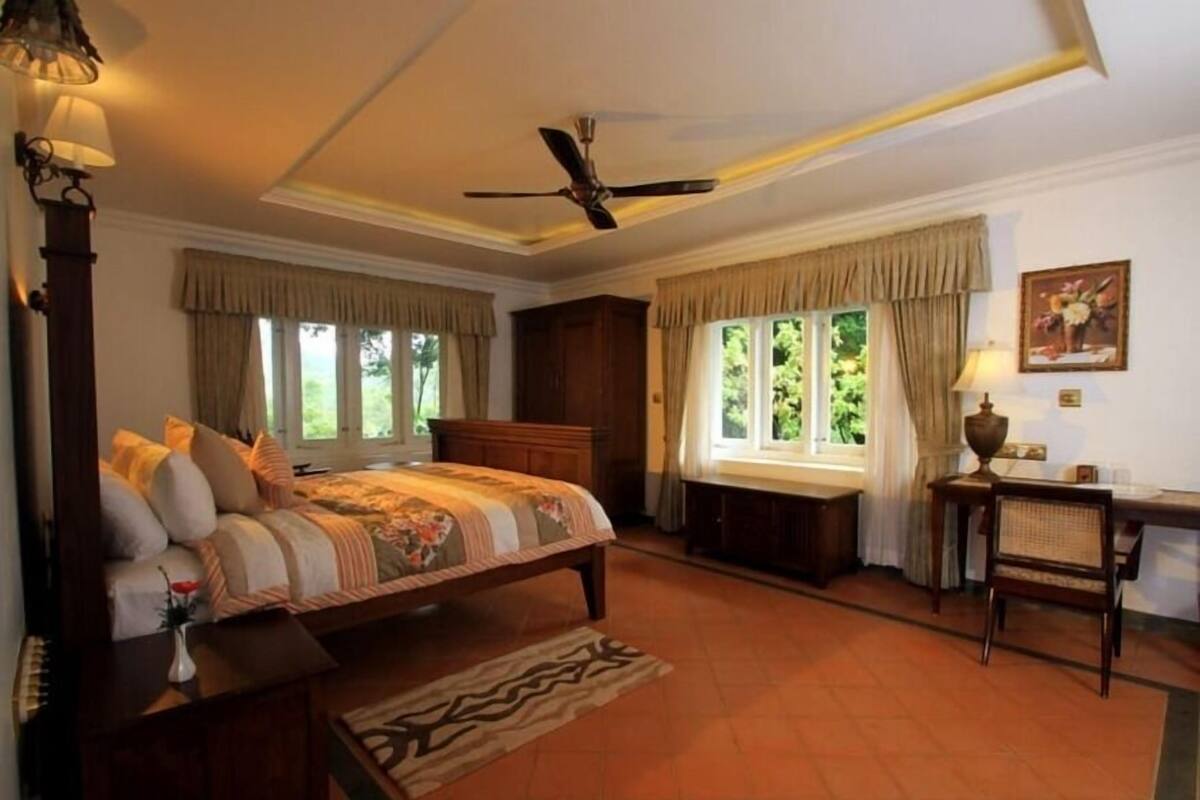 A bedroom with a bed, a desk, a chair, a ceiling fan, and windows with curtains.