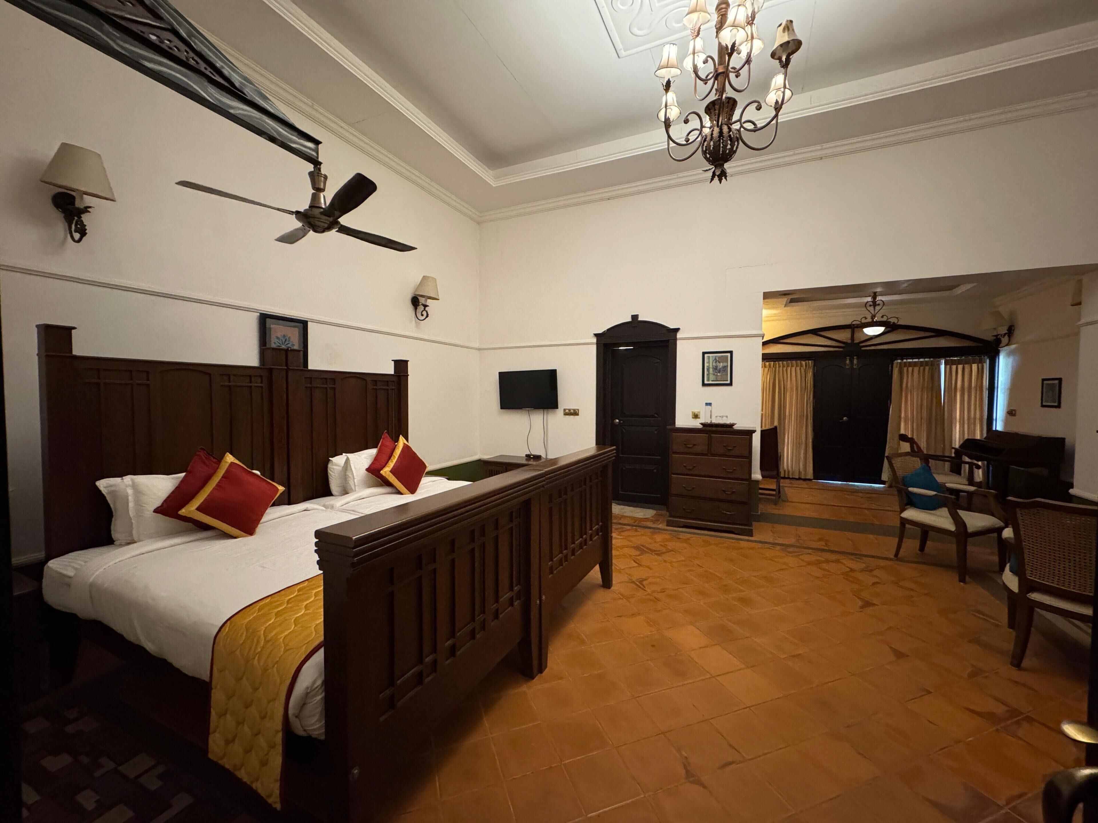 A hotel room with a large bed, a ceiling fan, a chandelier, a television, and a wooden dresser.