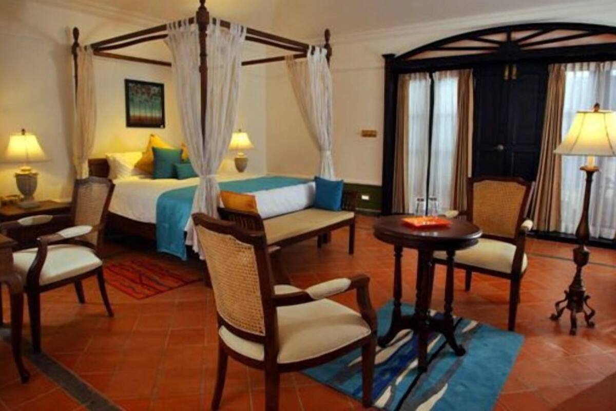 A hotel room with a four-poster bed, two bedside tables, a desk, a chair, and a small table with a lamp.
