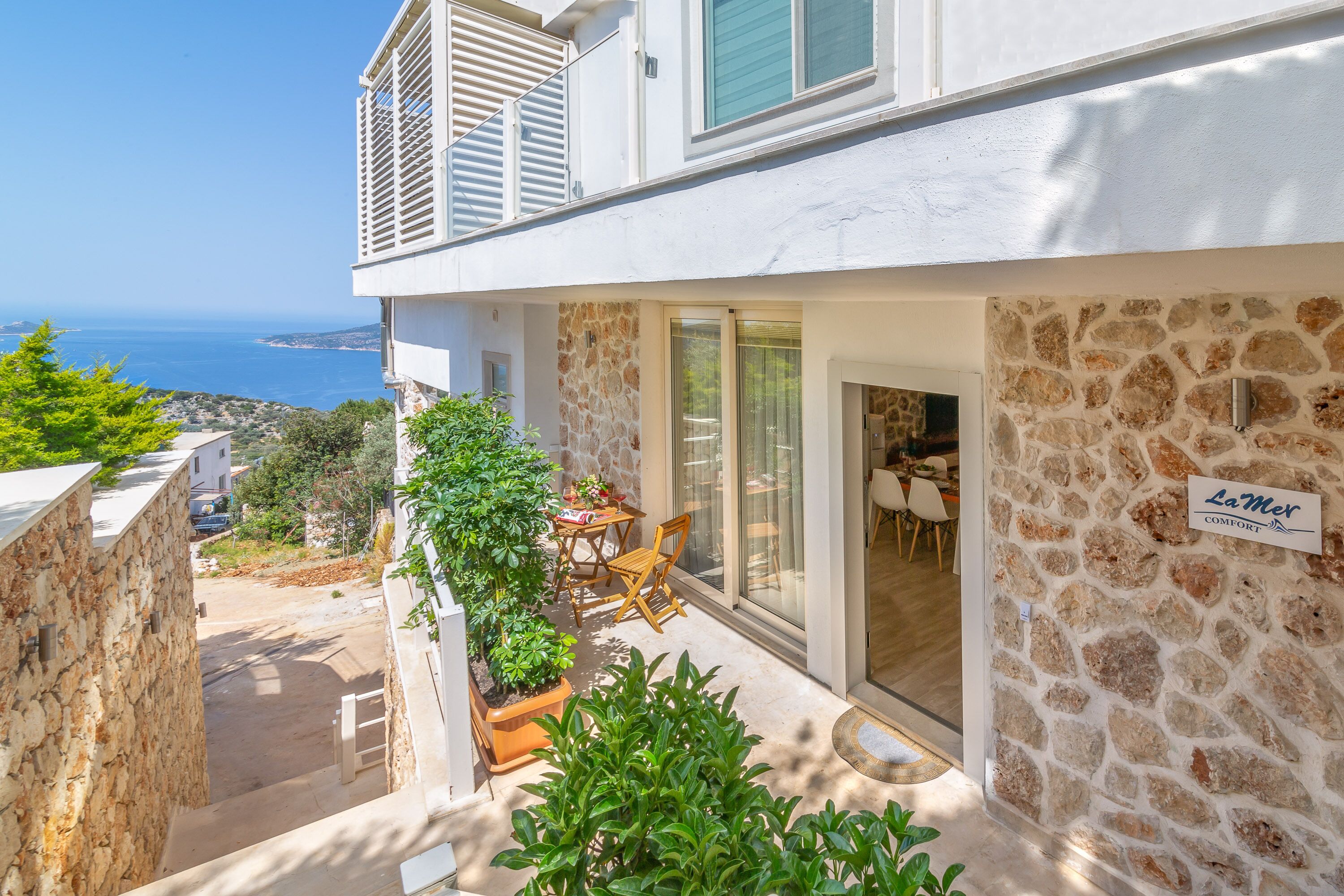 A modern building with a stone facade, a patio with outdoor furniture, and a view of the sea.