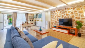 A modern living room with a large sofa, a TV on a wooden stand, and a kitchen in the background. - La Mer Comfort Kalkan (Kalkan - Kaş)