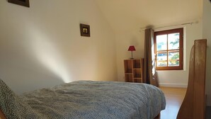 Ein Schlafzimmer mit einem gemusterten Bettbezug, einem Holzschrank, einer roten Lampe und einem Fenster mit Vorhängen.